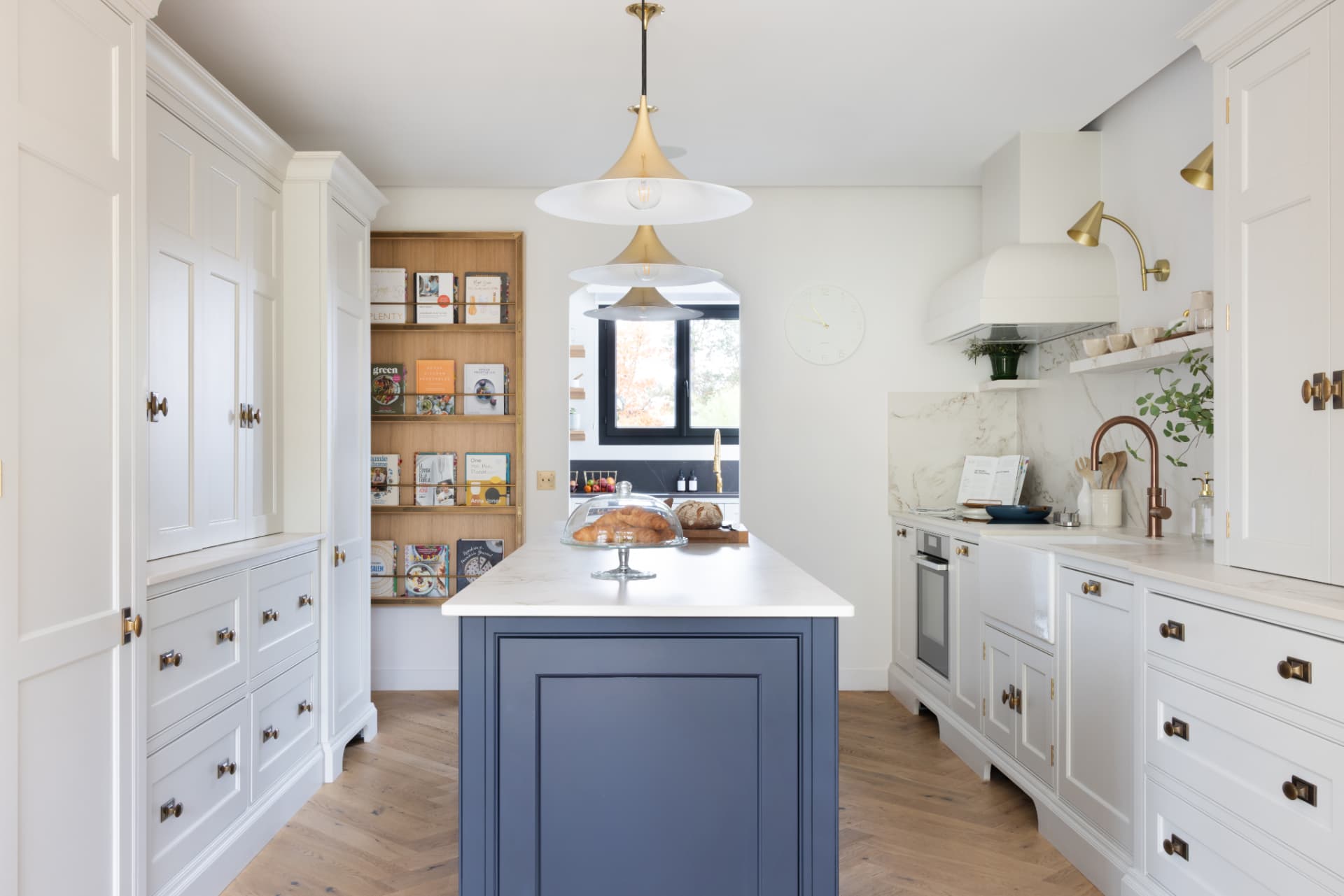 Lake Geneva House — symmetrical view of a bright kitchen with a navy island, marble worktop and brass pendant lights