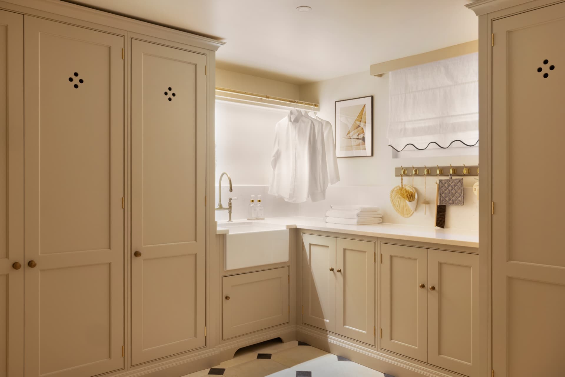 Lake Geneva House — laundry room with taupe cabinetry, farmhouse sink, brass hanging rail and chequerboard stone floor