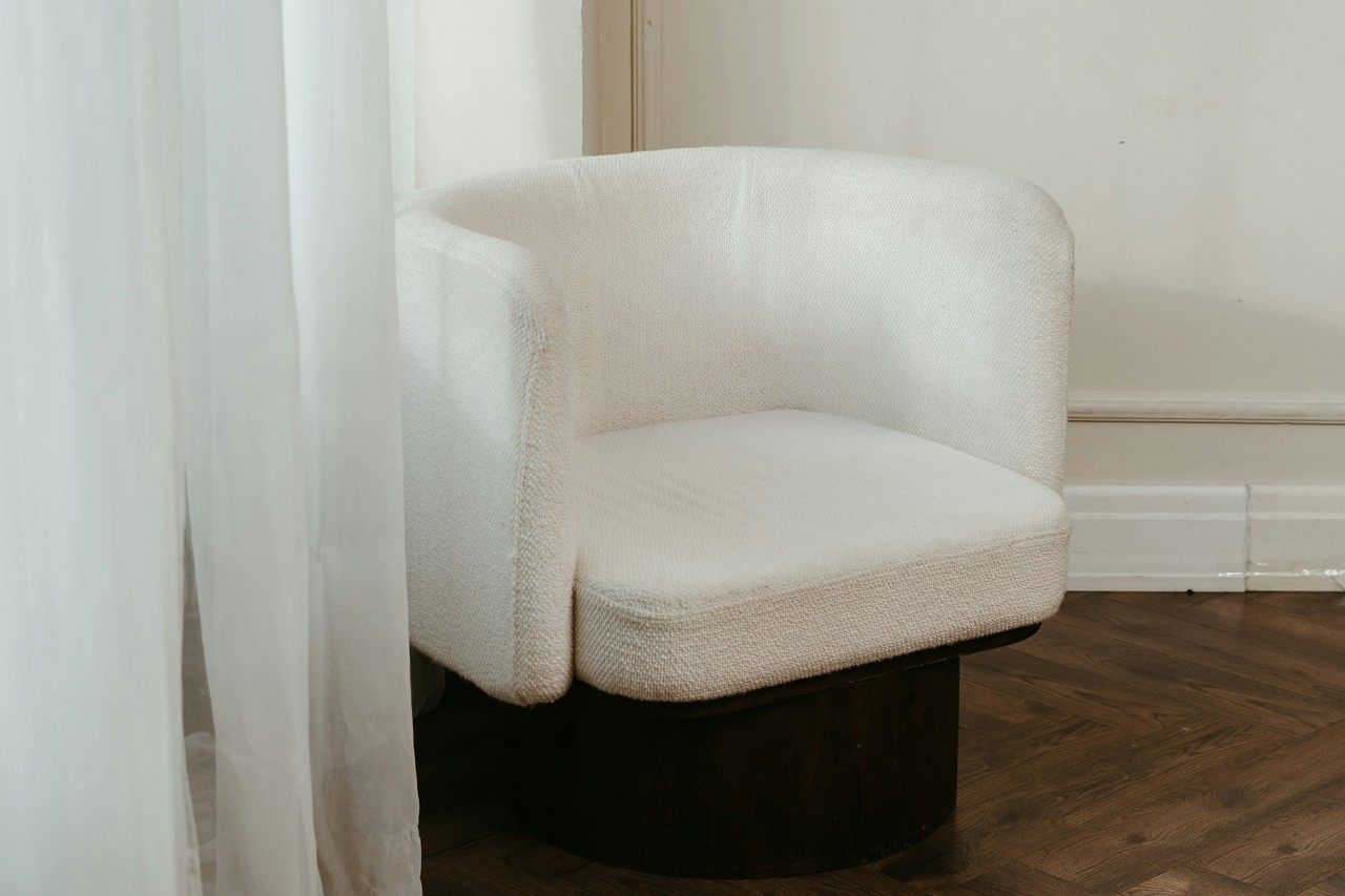 Granges Apartment — cream bouclé armchair with shell cushion beside sheer curtains and herringbone oak flooring